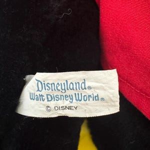 May include: Close-up of a plush toy with black fur and a red fabric element. A white tag displays the text "Disneyland Walt Disney World" and the Disney copyright symbol.