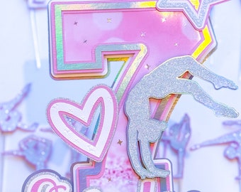 May include: Pink and silver glitter cake topper with a number 7, a gymnast silhouette, a heart, a star, and the word "Sweden".