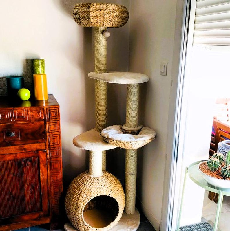May include: A tall cat tree with a natural woven base, a beige platform, and a woven sphere with a hole. The cat tree has multiple levels and scratching posts.