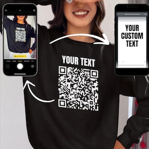 May include: Black sweatshirt with a white QR code and the text "YOUR TEXT" printed on the front. The sweatshirt is being modelled by a person.