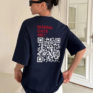 Könnte beinhalten: Ein dunkelblaues T-Shirt mit kurzen Ärmeln, das auf der Rückseite den roten Schriftzug "WANNA DATE ME?" über einem großen weißen QR-Code zeigt. Das T-Shirt hat einen Rundhalsausschnitt und eine lockere Passform für einen lässigen Look.