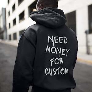 May include: Black hooded sweatshirt with the text "NEED MONEY FOR CUSTOM" printed in white on the back.