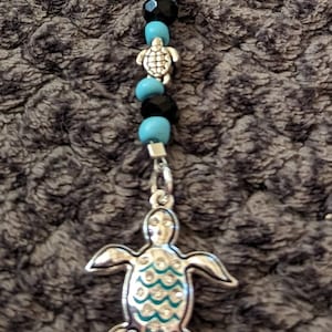 May include: A silver turtle charm with turquoise and black beads. The turtle has a detailed design with turquoise accents.