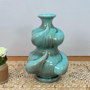 May include: A ceramic vase with a bulbous, multi-tiered silhouette and a narrow neck. The surface features a glossy glaze in shades of turquoise and teal, with blended brown accents highlighting the curved, organic, swirling forms.
