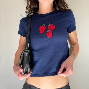 May include: A navy blue cropped t-shirt with a graphic of three red strawberries.