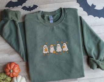 May include: A sage green sweatshirt with an embroidered design of four cartoon ghosts holding pumpkins. The ghosts are white with orange accents, surrounded by orange leaves. Paper bats and pumpkins are in the background.