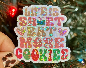 May include: A white sticker with a glittery finish and the text "Life is short eat more cookies". The sticker has a red, green, and brown color scheme and features a gingerbread cookie and a gift box.