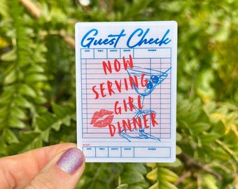 May include: A white sticker with a pink grid design, featuring the words "Guest Check" in blue script. The sticker also includes the text "Now Serving Girl Dinner" in red, along with a martini illustration and a pair of red lips.
