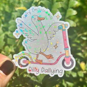 May include: A holographic sticker showing a cartoon goose on a pink scooter. The goose has its wings spread and the text reads "Sorry I'm late was dilly dallying". The sticker has a glitter effect and star details.