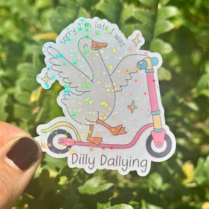 May include: A holographic sticker showing a goose on a pink scooter. The text reads "Sorry I'm late I was Dilly Dallying". The goose has its wings spread and is smiling. The sticker has a glittery effect.