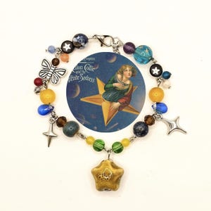 May include: A beaded bracelet with a variety of colorful beads, including yellow, blue, and green. The bracelet features a star-shaped charm and a silver butterfly charm. A circular image of a woman on a star is in the center.