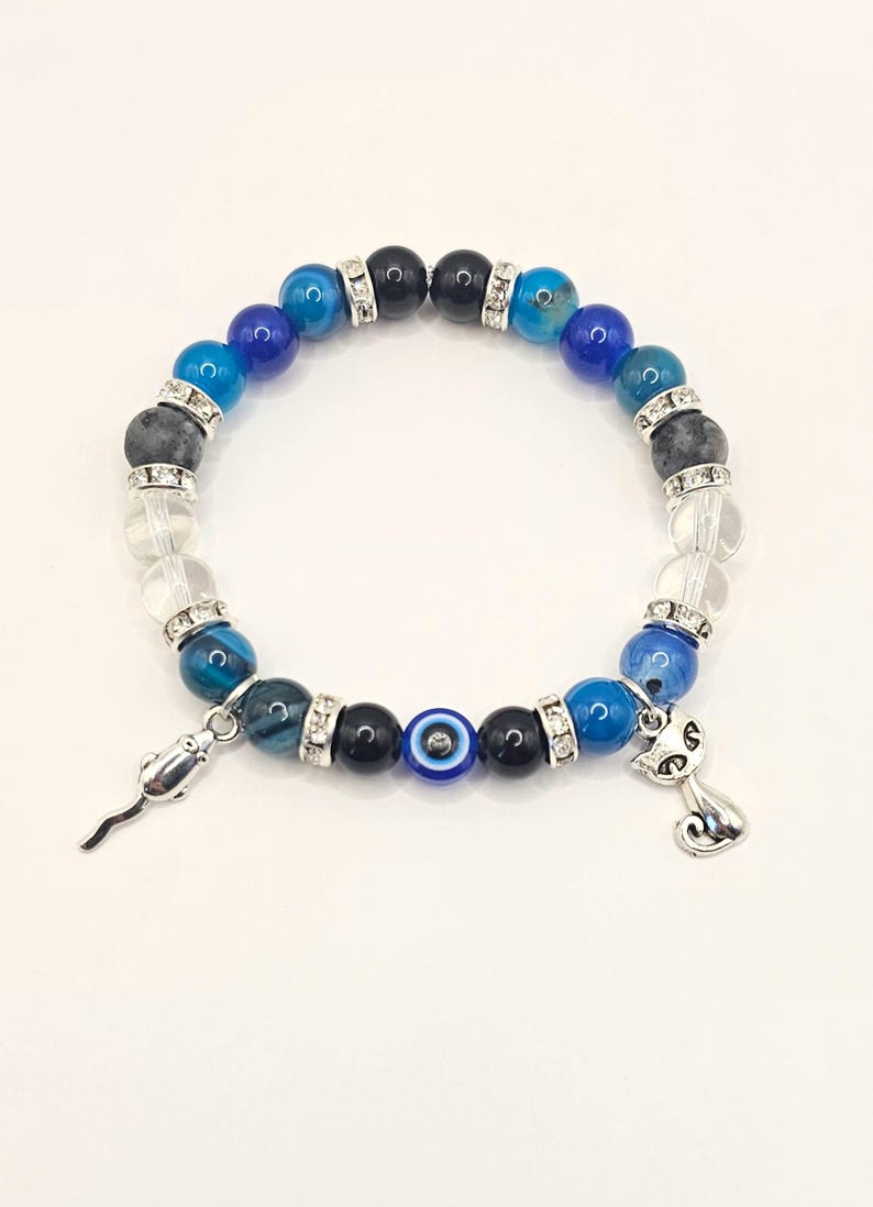 May include: A blue and black beaded bracelet with a silver charm of a cat and a silver charm of a mouse. The bracelet also features a blue evil eye bead.