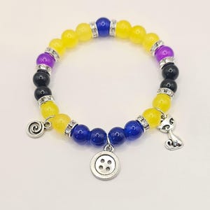 May include: A yellow, blue, and purple beaded bracelet with silver charms, including a button, a cat, and a swirl.