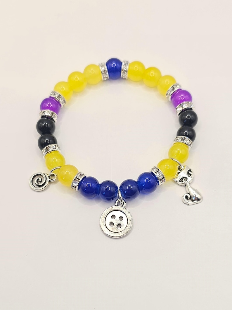 May include: A yellow, blue, and purple beaded bracelet with silver charms, including a button, a cat, and a swirl.