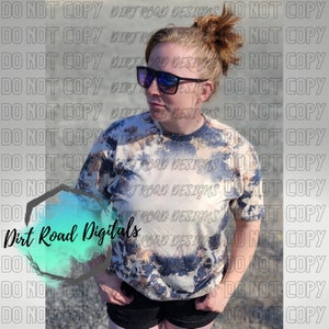 May include: A woman wearing a light blue and brown tie-dye shirt with the text "Dirt Road Digitals" on the front. She is wearing black shorts and sunglasses.