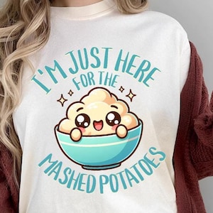 May include: Cream-colored t-shirt with the text "I'M JUST HERE FOR THE MASHED POTATOES" and a cartoon mashed potato design in a blue bowl. The shirt is worn with a burgundy cardigan and blue jeans.
