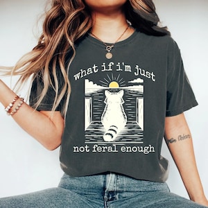 May include: A dark gray t-shirt with a graphic of a raccoon sitting on a porch with the text "what if i'm just not feral enough".