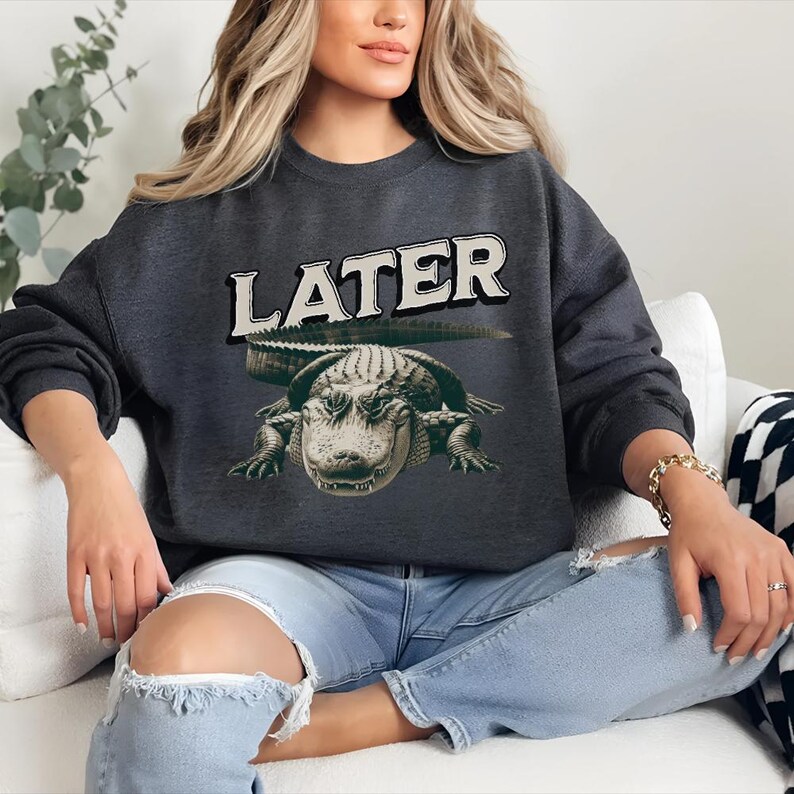 May include: A dark gray sweatshirt with a graphic of an alligator and the word "LATER" printed in white.