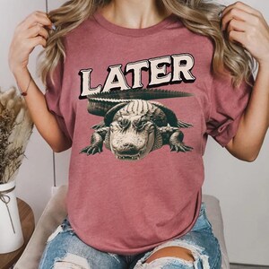 May include: A maroon t-shirt with a graphic of an alligator and the word "LATER" printed on it.