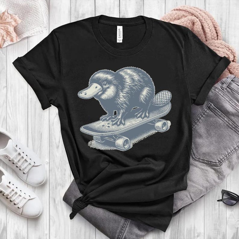 May include: Black t-shirt with a graphic of a platypus skateboarding. The platypus is blue and gray and the skateboard is gray.