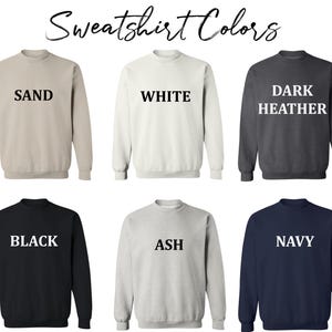 May include: Six different color sweatshirts with the color name printed in white on the front. The colors are sand, white, dark heather, black, ash, and navy.