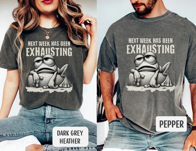 May include: A dark grey heather t-shirt with the text "Next week has been exhausting" and a cartoon frog with a tired expression. The shirt is available in a pepper color.