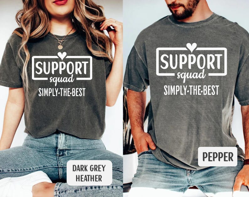 May include: Two dark grey t-shirts with the text "SUPPORT squad SIMPLY-THE-BEST" in a white rectangular box. One shirt is labeled "DARK GREY HEATHER" and the other is labeled "PEPPER". The shirts are worn by two people.