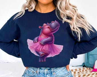 May include: A navy blue sweatshirt with a graphic of a pink hippopotamus wearing a pink tutu. The hippopotamus is smiling and has its arms raised in the air.
