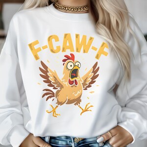 May include: White sweatshirt with a cartoon chicken graphic. The chicken is light brown with a red comb and open beak, arms outstretched. Above the chicken is the text "F-CAW-F" in yellow.