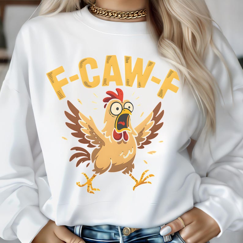 May include: White sweatshirt with a cartoon chicken graphic. The chicken is light brown with a red comb and open beak, arms outstretched. Above the chicken is the text "F-CAW-F" in yellow.