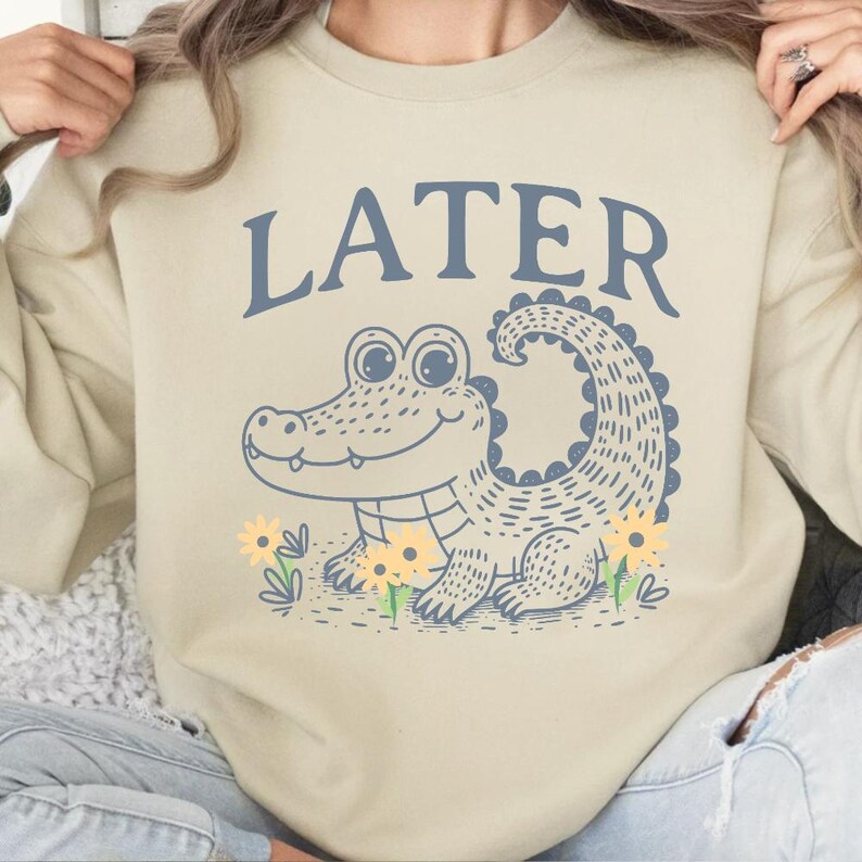 May include: A beige sweatshirt with a blue alligator graphic and the word "LATER" in blue text.