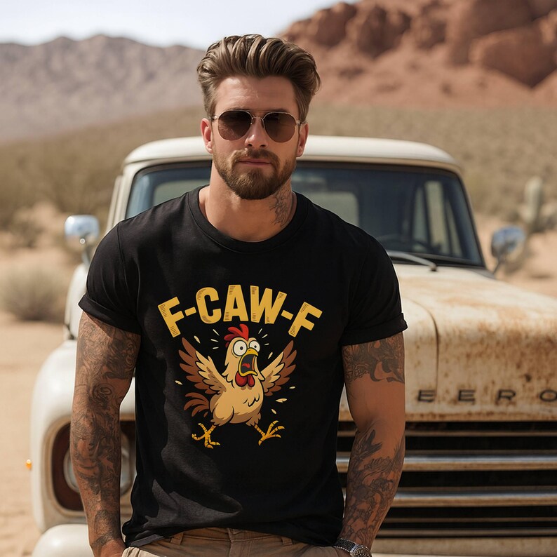 May include: Black t-shirt with the text "F-CAW-F" in yellow above a cartoon chicken with open wings and a surprised expression. The shirt is worn by a person with tattoos, sunglasses, and a beard.