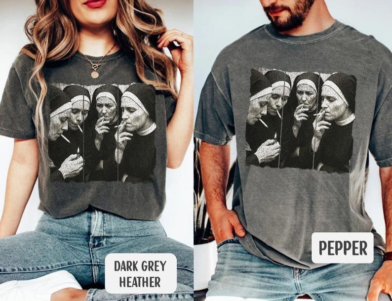 May include: Dark grey heather and pepper-colored t-shirts featuring a black and white graphic of four nuns smoking cigarettes. The image is printed on the front of the shirts. The shirts are displayed on two people.