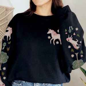 May include: Black sweatshirt with a unicorn and floral design on the sleeves. The sweatshirt is made of a soft, comfortable material.