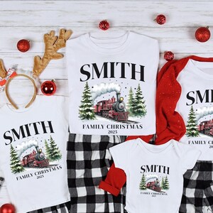 May include: White family Christmas shirts with a train graphic, the family name "SMITH", and "Family Christmas 2025". The shirts are paired with black and white plaid pajama pants. Red accessories and reindeer antlers are also present.