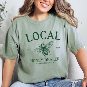May include: A green t-shirt with the text "LOCAL" in green, a bee illustration, and the text "EST. 2024 HONEY DEALER SAN FRANCISCO, CA".