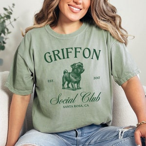 May include: A green t-shirt with the text "GRIFFON Social Club" and a pug illustration. The text "EST. 2017" and "SANTA ROSA, CA" are also printed on the shirt.