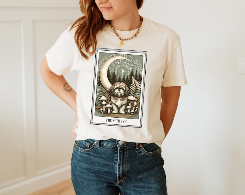 May include: A white t-shirt with a graphic of a Shih Tzu dog in a forest setting with a crescent moon and stars. The text "THE SHIH TZU" is printed below the image.