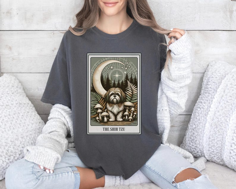 May include: A dark gray t-shirt with a graphic of a Shih Tzu dog sitting in a forest with mushrooms and a crescent moon. The text "THE SHIH TZU" is printed below the graphic.