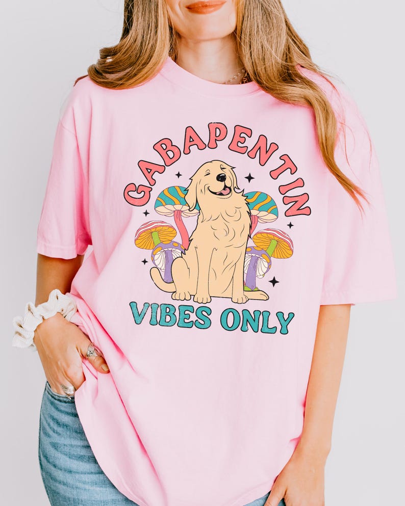 K&ouml;nnte beinhalten: Pinkes T-Shirt mit einem Grafikdruck eines Golden Retriever Hundes, der vor bunten Pilzen sitzt. Der Text "Gabapentin Vibes Only" ist auf dem Shirt aufgedruckt.
