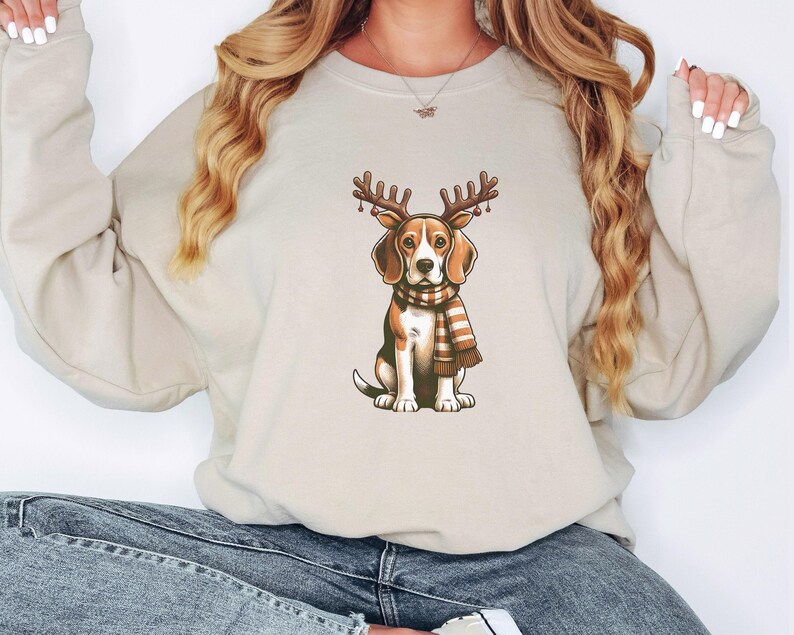 May include: A beige sweatshirt with a graphic of a beagle wearing a red and white reindeer antler headband and a brown and white striped scarf.