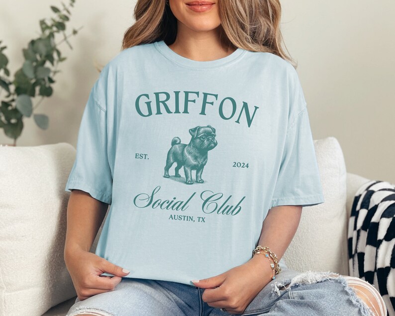 May include: Light blue t-shirt with a green graphic of a pug wearing glasses. The graphic says "Griffon Social Club Est. 2024 Austin, TX"