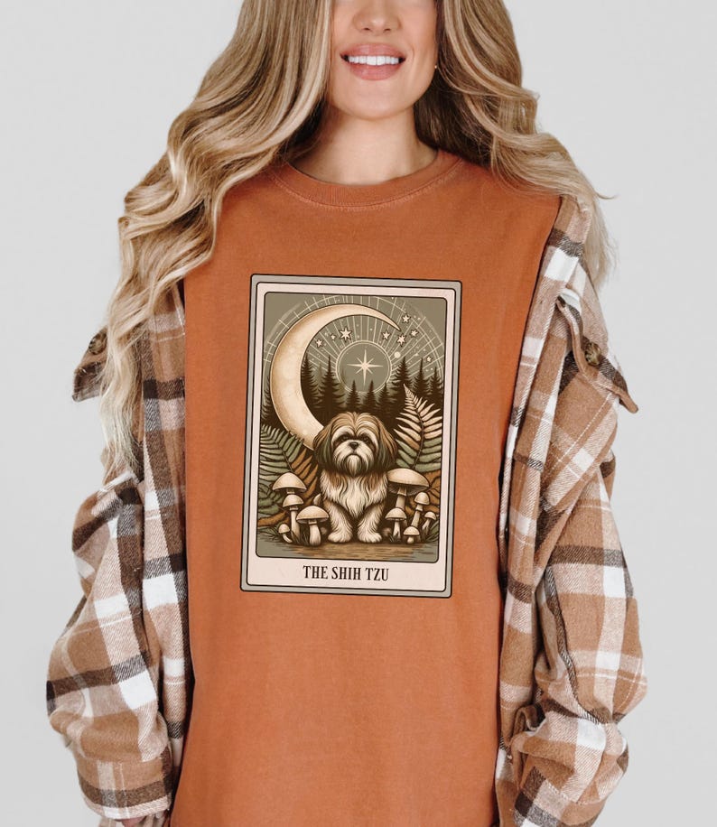 May include: A rust-colored t-shirt with a graphic of a tarot card featuring a Shih Tzu dog sitting in a forest with a crescent moon and stars above. The card reads "The Shih Tzu".