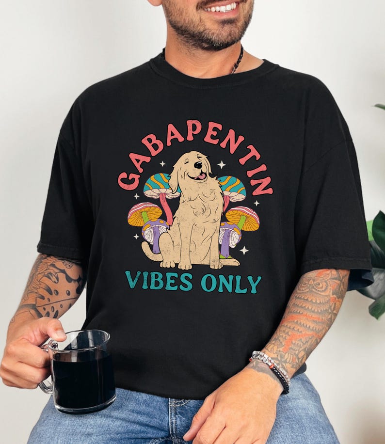 K&ouml;nnte beinhalten: Schwarzes T-Shirt mit einem Grafikdruck eines Hundes, der vor Pilzen sitzt. Der Text "Gabapentin Vibes Only" ist auf dem Shirt aufgedruckt.