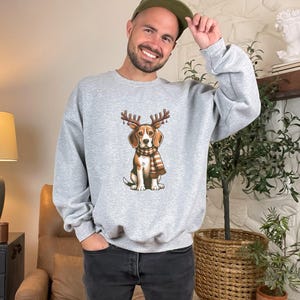 May include: A gray sweatshirt with a cartoon beagle wearing a scarf and antlers. The beagle is wearing a red and white scarf and has a brown nose and brown eyes.