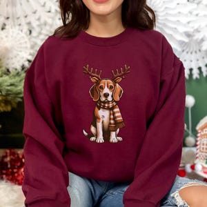 May include: A maroon sweatshirt with a graphic of a beagle wearing reindeer antlers and a plaid scarf. The beagle is looking directly at the viewer.