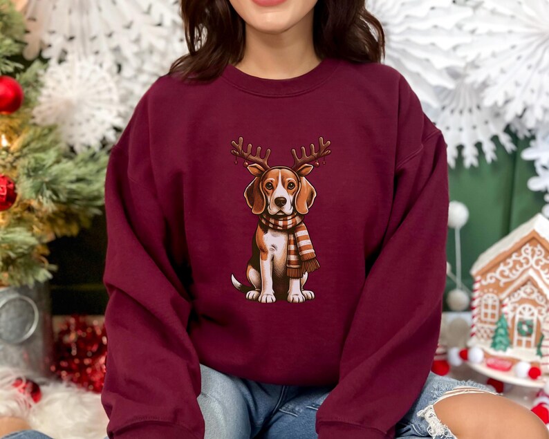 May include: A maroon sweatshirt with a graphic of a beagle wearing reindeer antlers and a plaid scarf. The beagle is looking directly at the viewer.