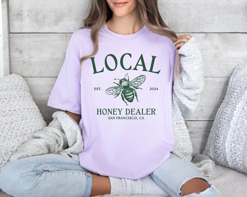 May include: A lavender t-shirt with a green bee graphic and the text "LOCAL EST. 2024 HONEY DEALER SAN FRANCISCO, CA"