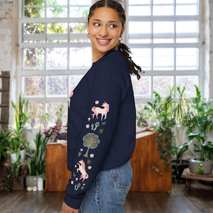 May include: A navy blue long-sleeved sweatshirt with a pink unicorn and floral design on the sleeve. The sweatshirt is made of a soft, comfortable material.