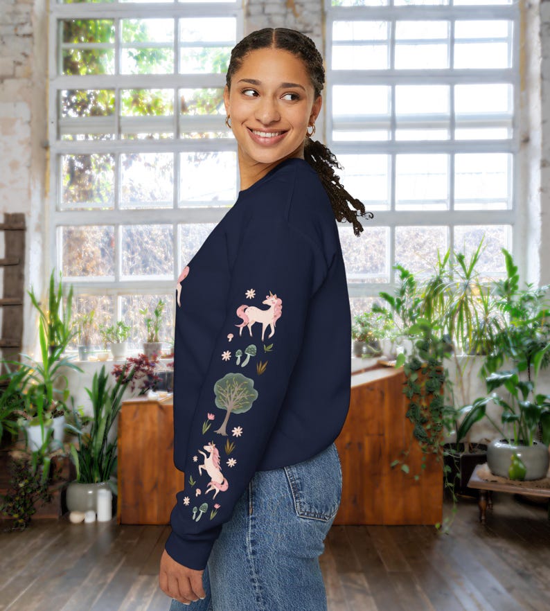 May include: A navy blue long-sleeved sweatshirt with a pink unicorn and floral design on the sleeve. The sweatshirt is made of a soft, comfortable material.